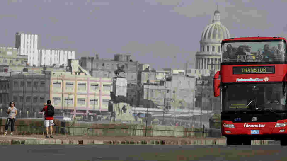 Tourists take photos as a sightseeing bus drives by along Havana's Malecon