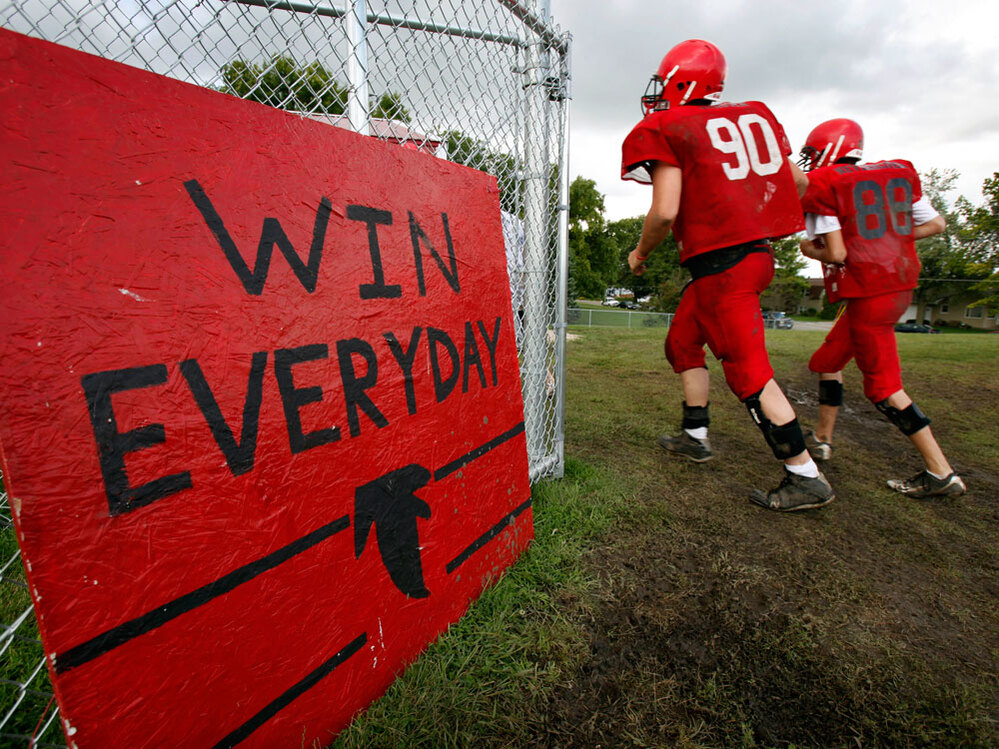'Win Everyday': Aplington-Parkersburg High football players run past a sign on the practice field