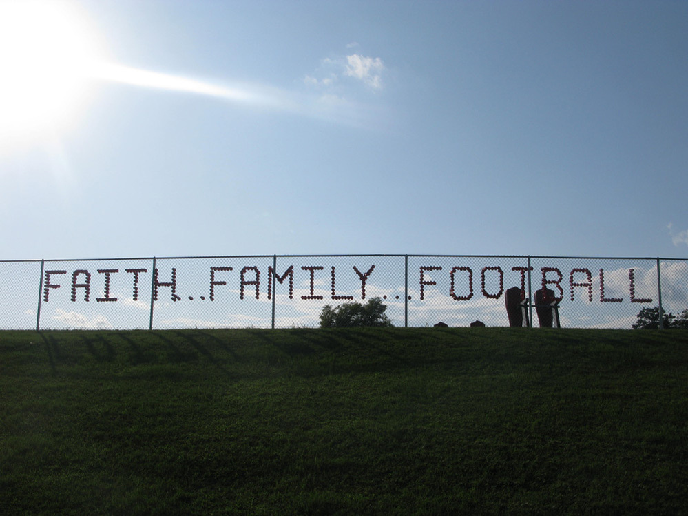 Red plastic cups stuck in a chain-link fence spell out faith, family, football.