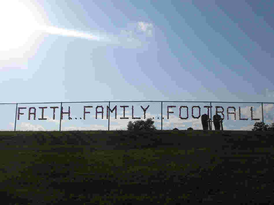 Red plastic cups stuck in a chain-link fence spell out faith, family, football.
