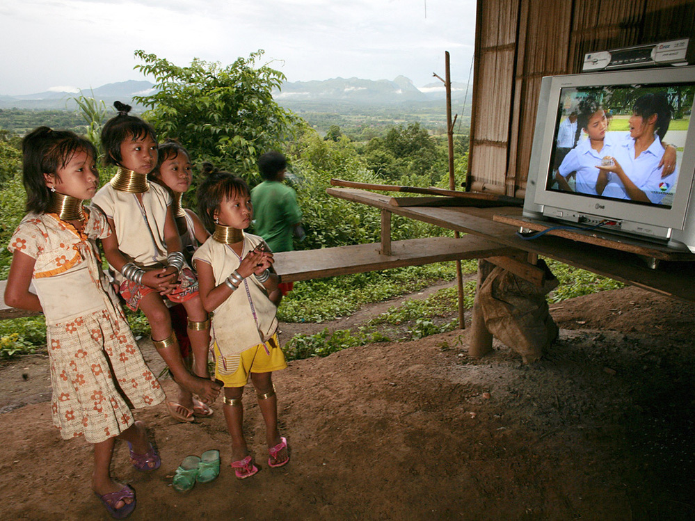 Young girls of the Long Neck Padaung hill tribe watch television in a small village in Chiang Dao, T
