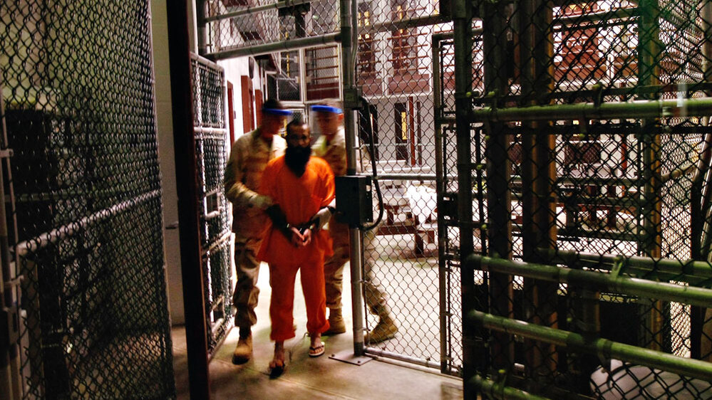 A wide view of a 'noncompliant' detainee escorted by guards at Guantanamo Bay