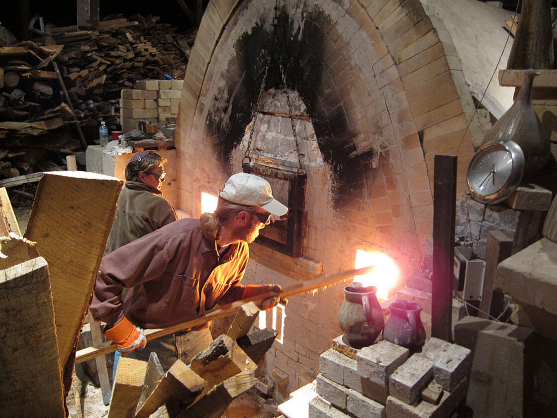 Volunteers Nancy Parent and Dan Corwin-Renner stoke the kiln.