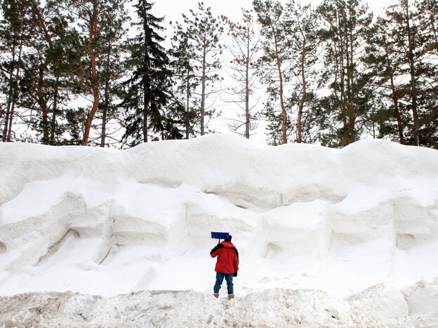 A man stands with a shovel before a snow pile.