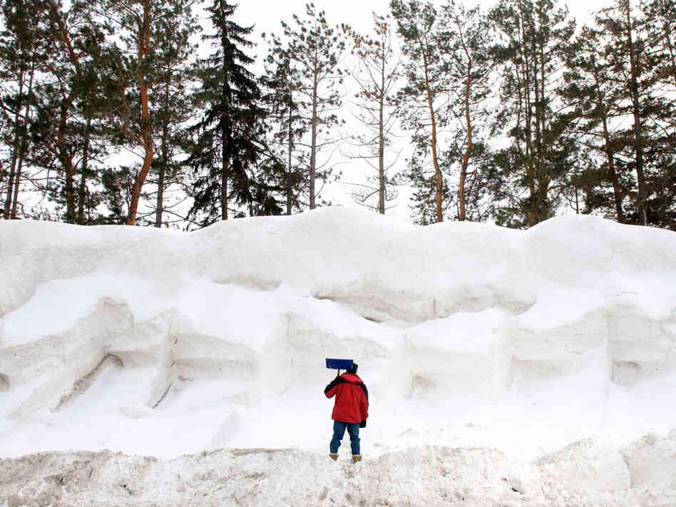 A man stands with a shovel before a snow pile.