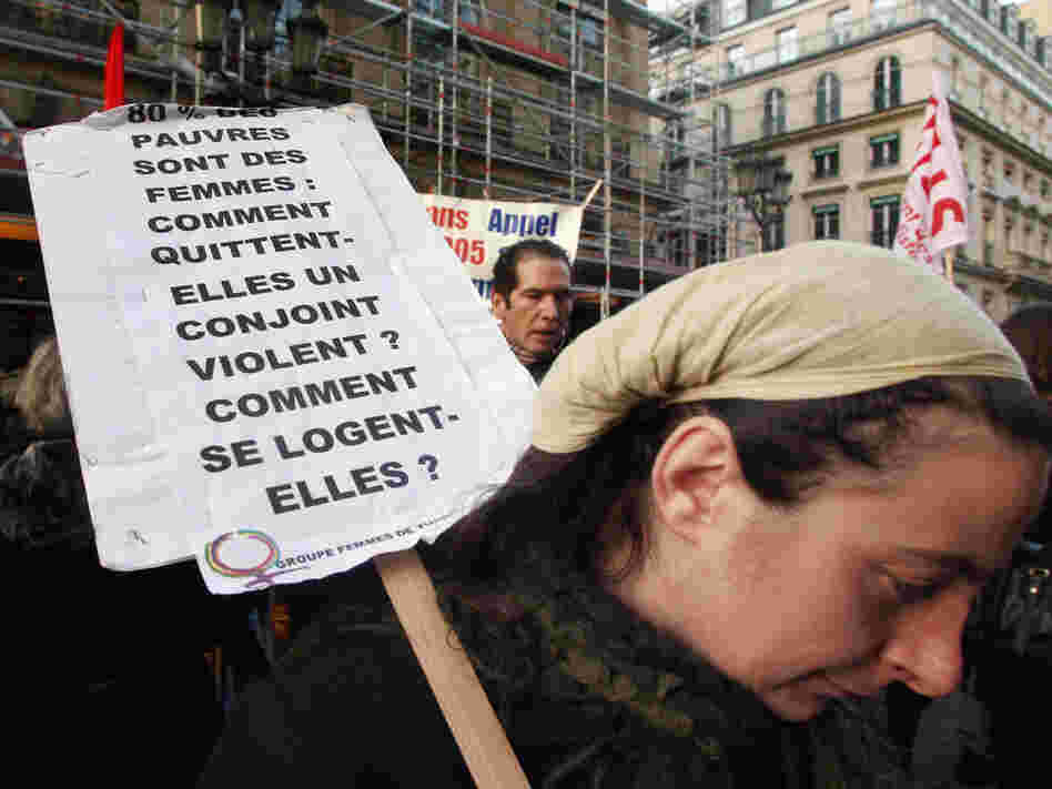 A woman holds a banner which refers to poor, powerless women facing domestic violence.