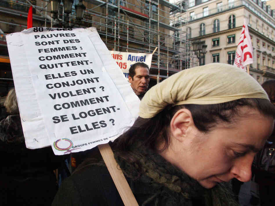 A woman holds a banner which refers to poor, powerless women facing domestic violence.