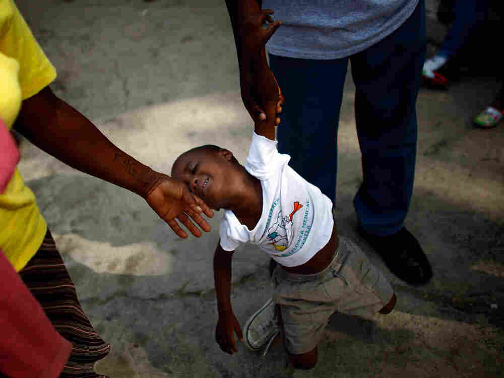 A boy slumps as two people try to move him along at an orphanage in Haiti A boy slumps as two people try to move him along at an orphanage in Haiti
