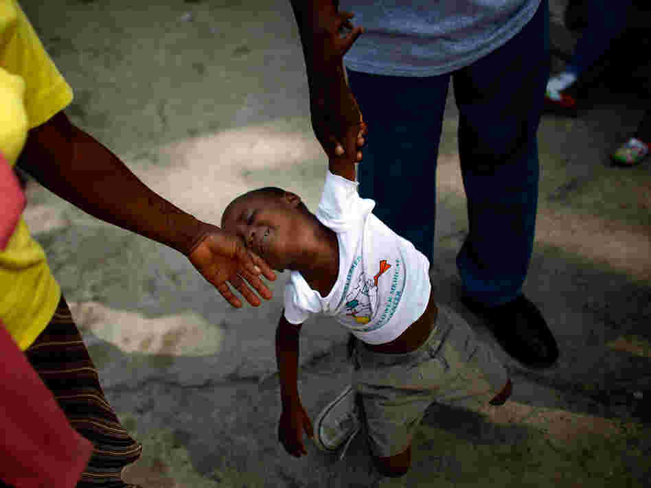 A boy slumps as two people try to move him along at an orphanage in Haiti A boy slumps as two people try to move him along at an orphanage in Haiti