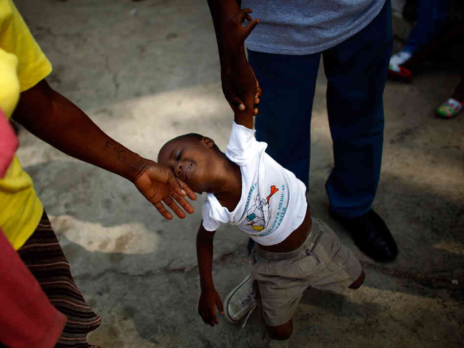 A boy slumps as two people try to move him along at an orphanage in Haiti A boy slumps as two people try to move him along at an orphanage in Haiti