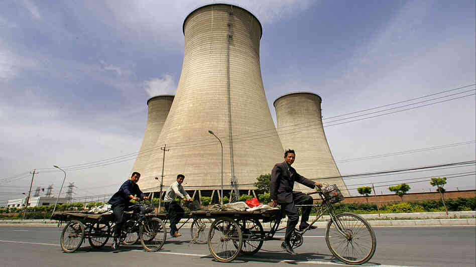 Workers in China bicycle past cooling towers of a coal-fired power plant. Workers in China bicycle past cooling towers of a coal-fired power plant.