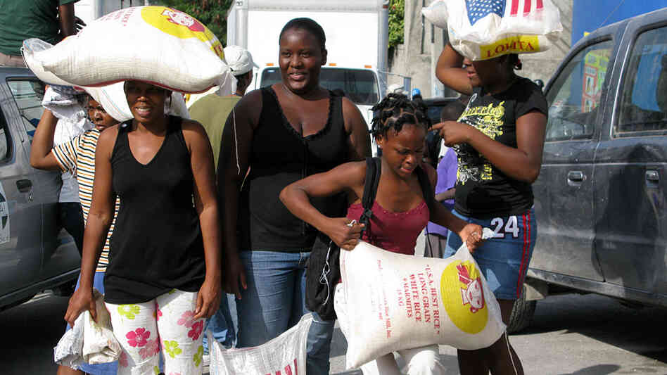 Women struggle to carry 55-pound bags of rice given out Sunday in Port-au-Prince, Haiti.