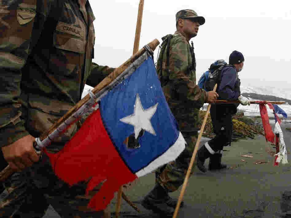 Soldiers and rescue workers carrying damaged Chilean flags search for victims.
