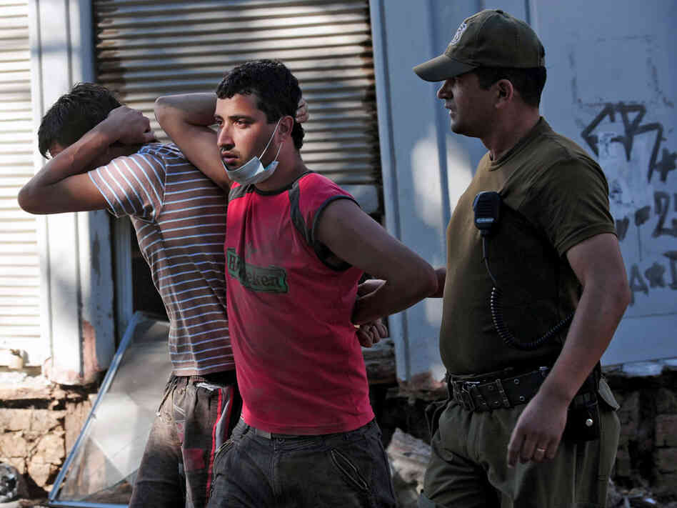 A soldier escorts two men detained for looting on Tuesday in the fishing village of Constitucion.