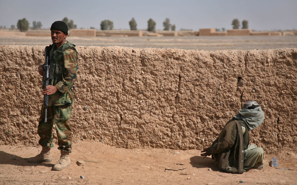 An Afghan National Army soldier stands guard over a blindfolded suspected Taliban fighter.