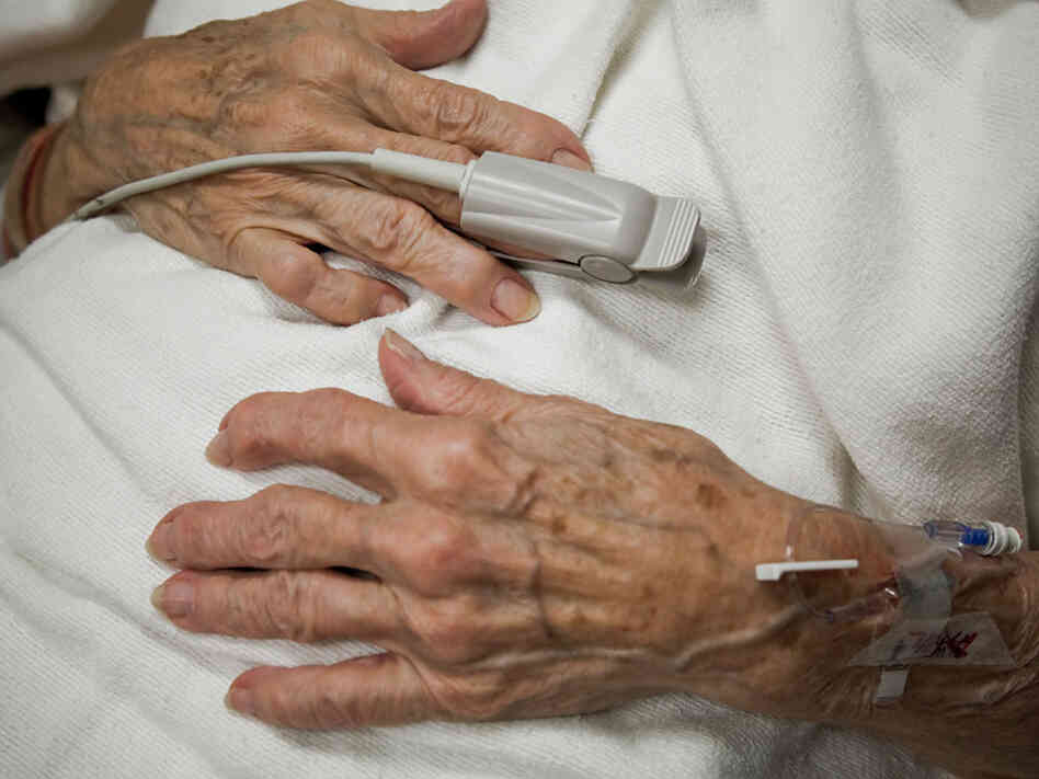 An older woman's hands on her lap as she lies in hospital bed. An older woman's hands on her lap as she lies in hospital bed.