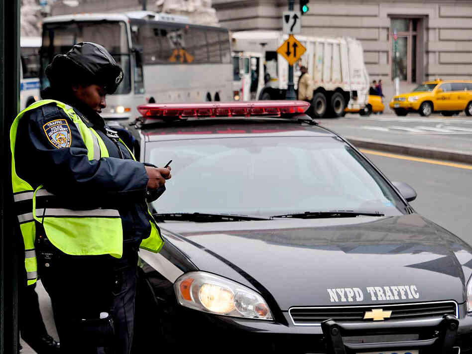 An NYPD officer uses a phone to send text messages on a New York sidewalk.