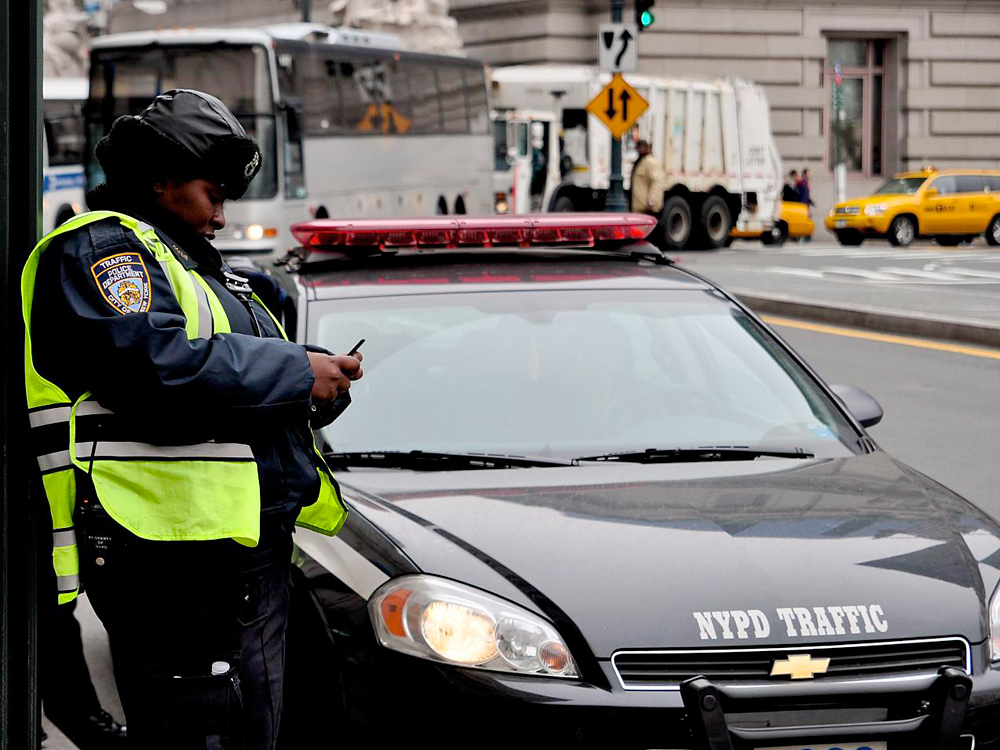 An NYPD officer uses a phone to send text messages on a New York sidewalk.