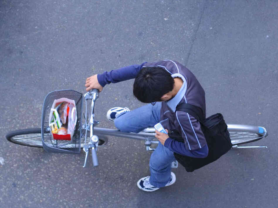 Youth on bicycle looks at cell phone.