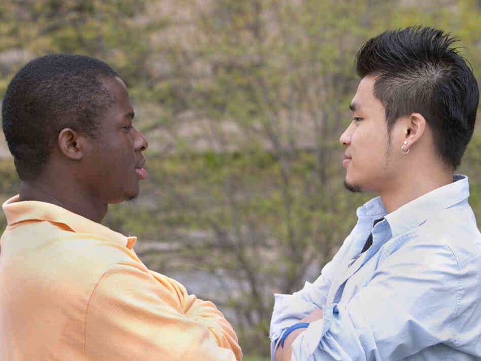 Two men, one black and one Asian, stare at each other