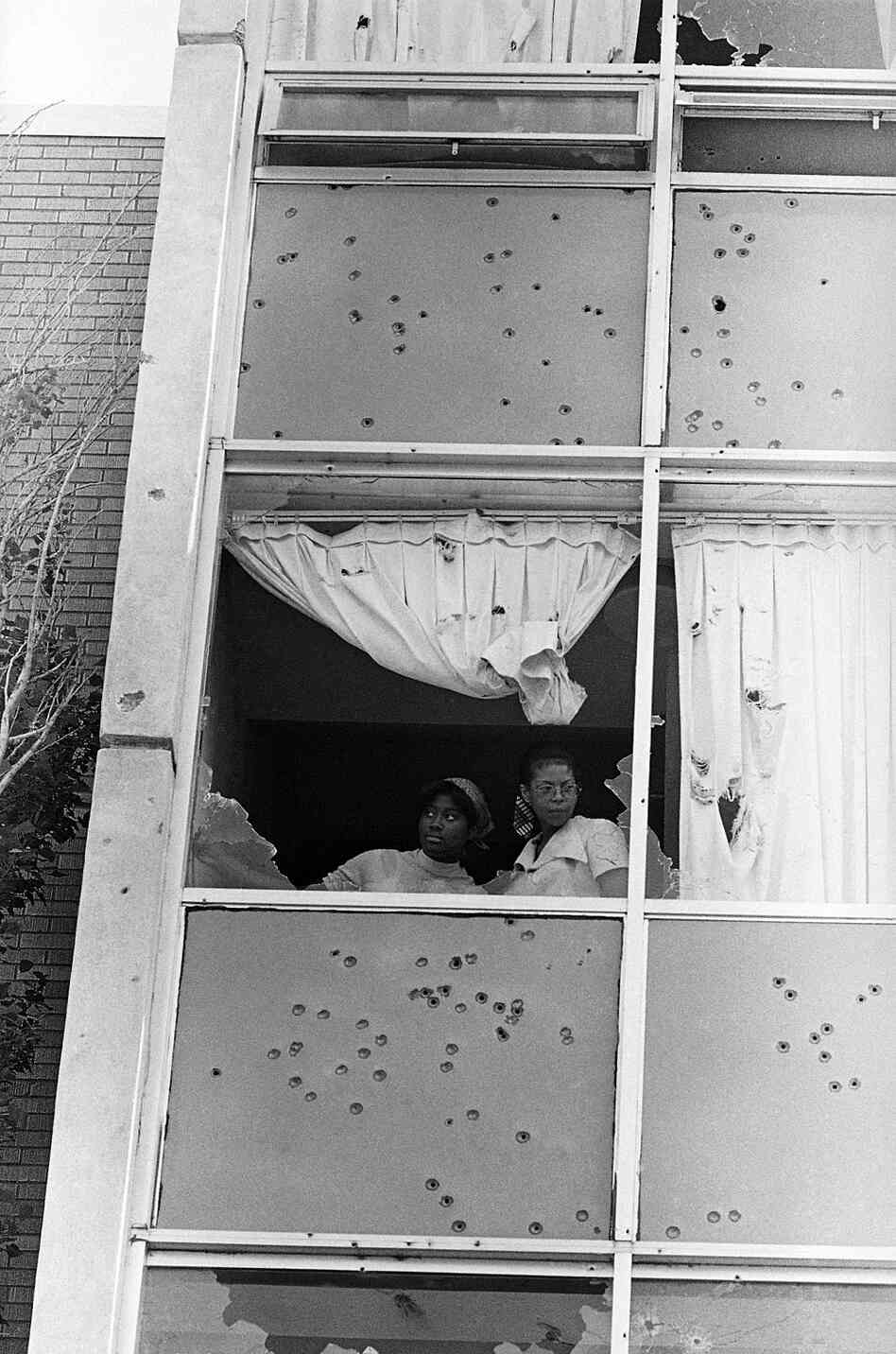 Two students at Jackson State College peer from a window that was shot out by police on campus.