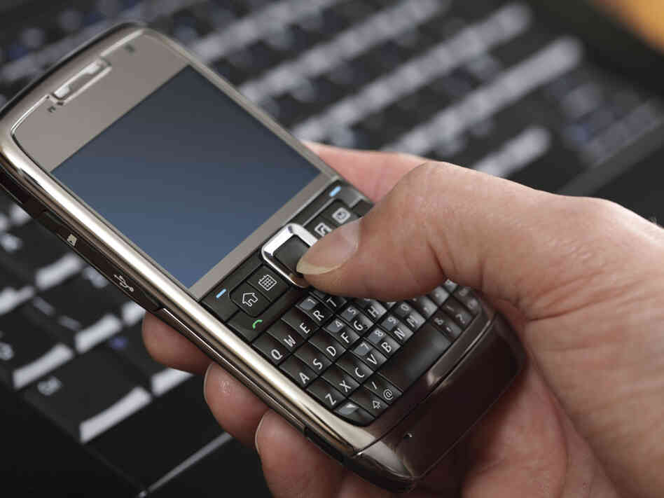 A consumer uses a smart phone near a laptop.