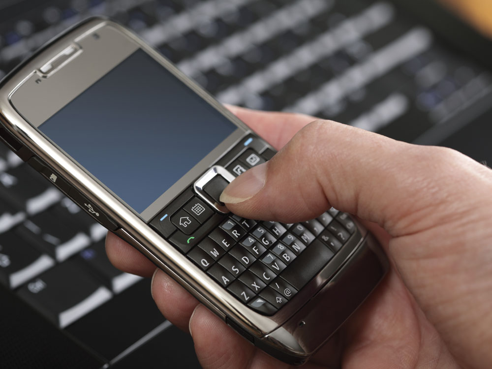 A consumer uses a smart phone near a laptop.