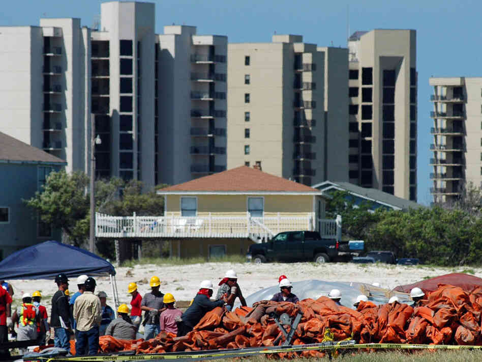Workers handle oil-blocking booms in Alabama with condominiums in the background