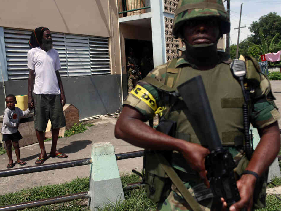Soldier patrols while resident of Tivoli Gardens neighborhood in Kingston looks on