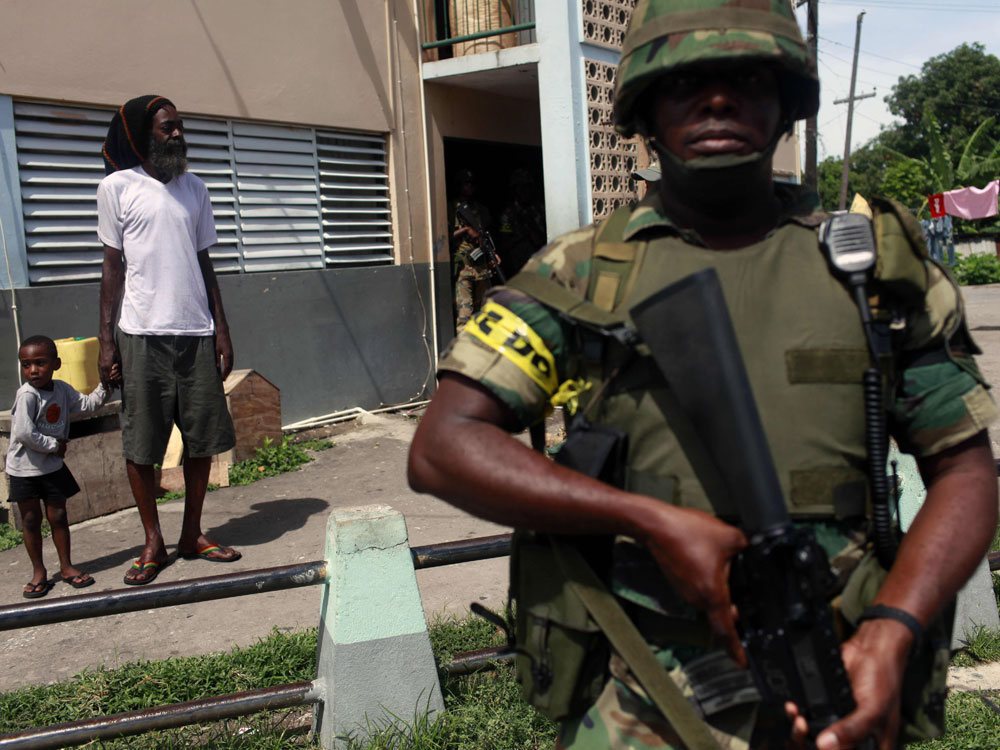 Soldier patrols while resident of Tivoli Gardens neighborhood in Kingston looks on