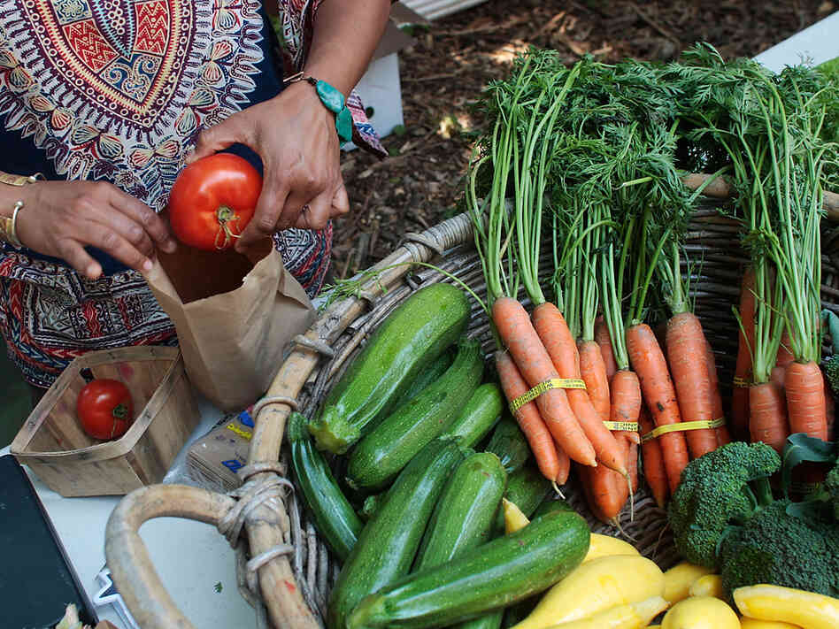 A woman bags fresh organic vegetables at a community farmers market.