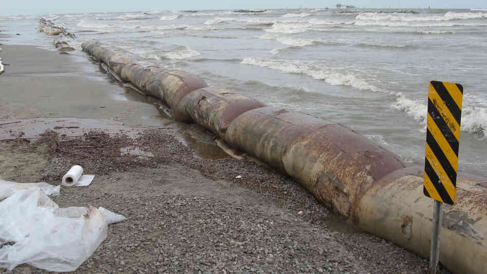 Oil-stained barriers sit on a Louisiana beach, with the surf breaking behind them