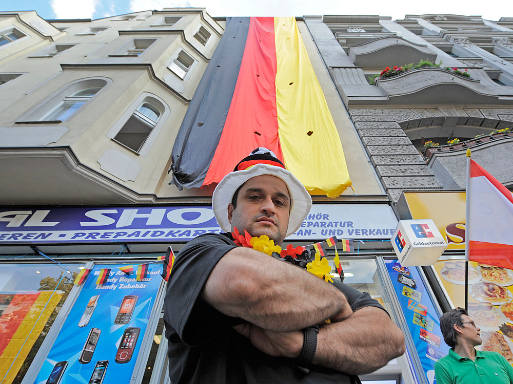 Beirut-born Ibrahim Bassal poses Tuesday near the four-story-deep German flag he has hung above his electronics shop in Berlin to show support for the German national soccer team, which plays in the World Cup quarterfinals Saturday. Displays of nationalism such as flag-waving and anthem-singing have renewed debate in Germany over the country's history of extreme patriotism.
