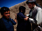 Afghan police officer (left) searches a man while local leader Karim Jan (right) holds his arms Afghan police officer (left) searches a man while local leader Karim Jan (right) holds his arms