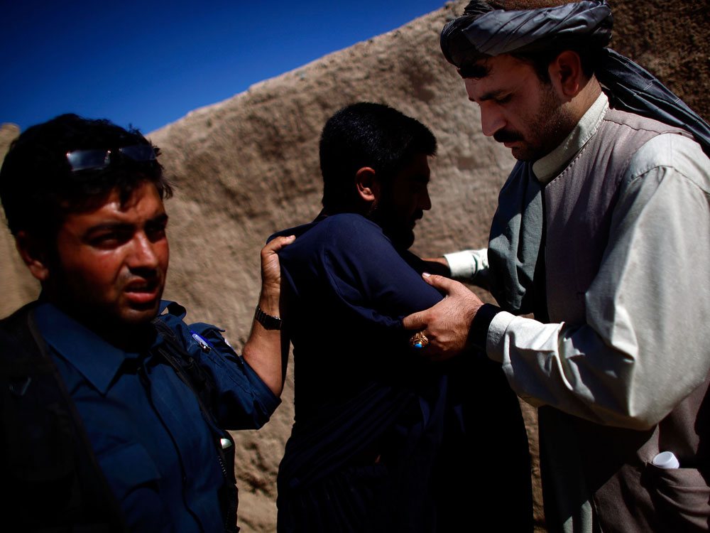 Afghan police officer (left) searches a man while local leader Karim Jan (right) holds his arms