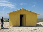 A guard stands outside a prototype "transitional" housing model at a resettlement camp. A guard stands outside a prototype "transitional" housing model at a resettlement camp.