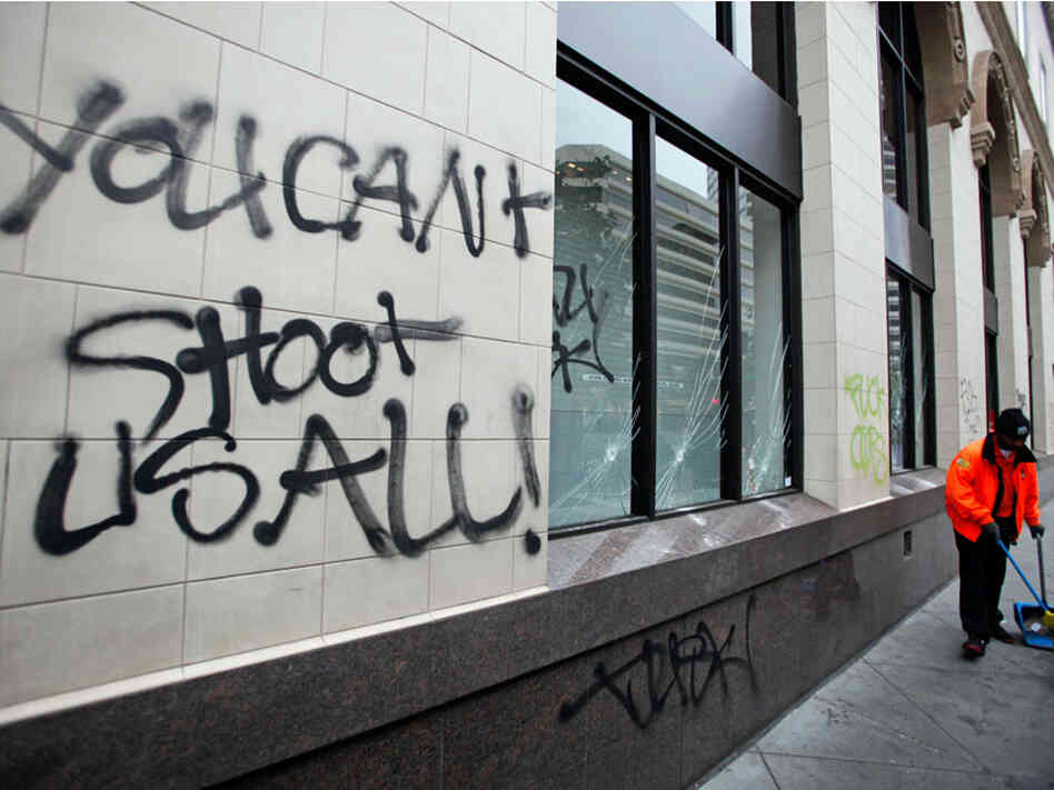 A worker sweeps the sidewalk near graffiti painted by protesters in downtown Oakland.