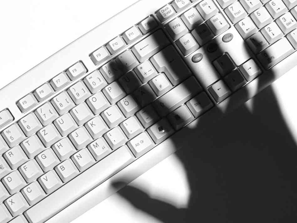 A shadowy hand hovers over a computer keyboard.