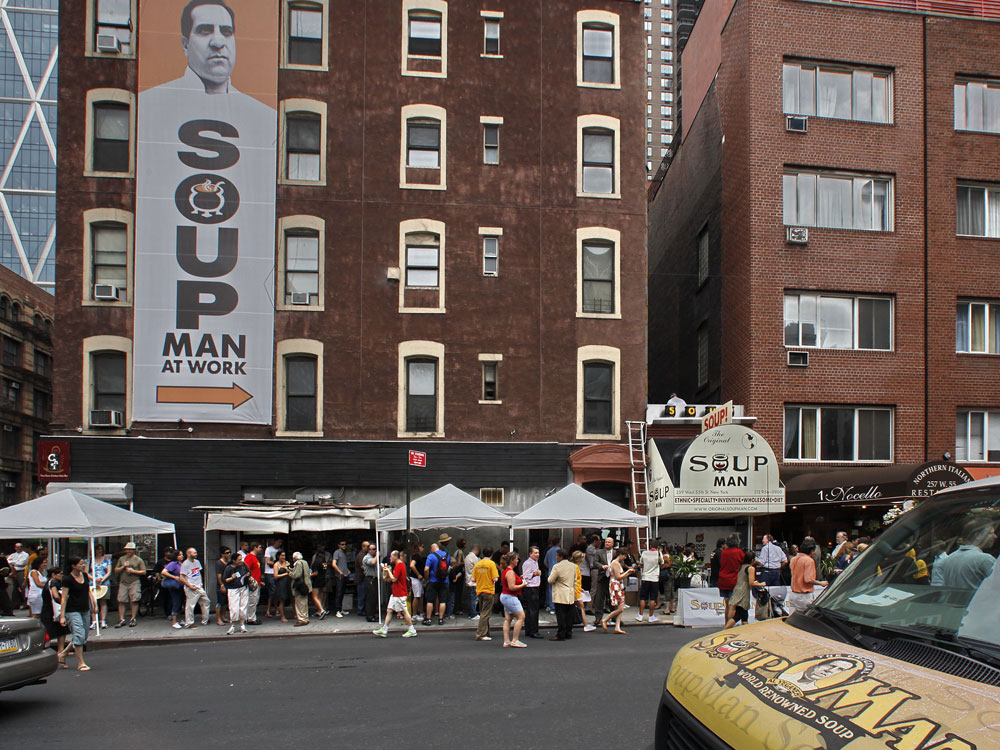 About 100 people stand in line for the reopening of the Original SoupMan gourmet takeout shop.