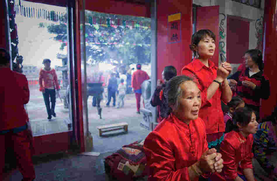 Women in lucky red outfits light incense and bow to Mazu the night before her birthday celebration Women in lucky red outfits light incense and bow to Mazu the night before her birthday celebration