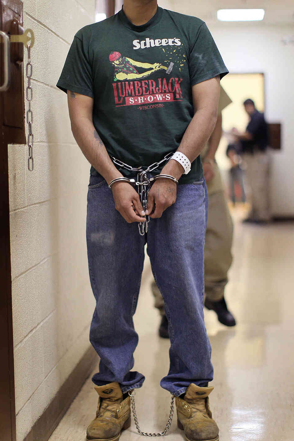An man wearing handcuffs waits to be deported