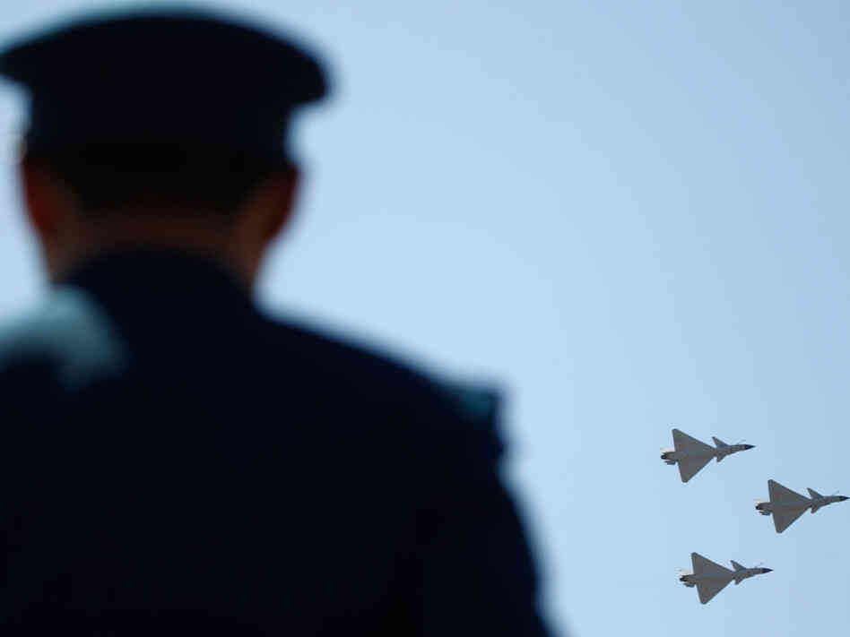 Chinese J-10 fighter jets fly-by in formation as an air force personnel stands guard