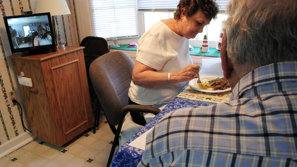 Edward and Lavinia Fitzgerald in Savannah, Ga., have dinner while telecaregiver Denise Cady of ResCare, a camera monitoring service, looks on.