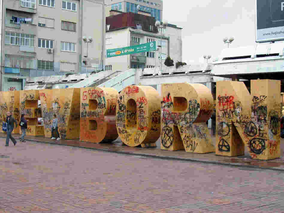 Pedestrians walk past graffiti-covered street art in Kosovo.