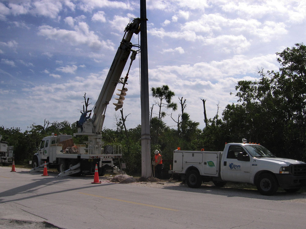 A work crew installs a concrete power pole on the island.