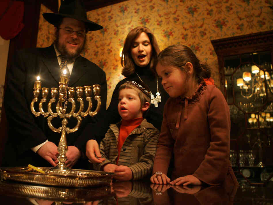 Rabbi Joshua Metzger, his wife Brocha, and their children Menachem Mendel and Sarah Perel stand by a menorah.