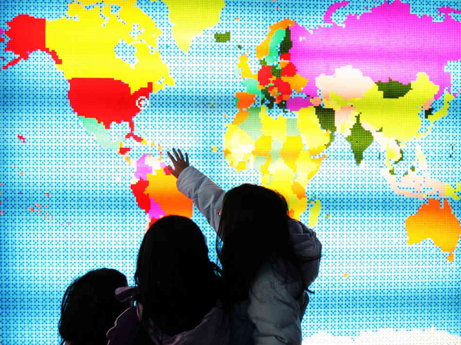 Children touching a lit up map of the world. Children touching a lit up map of the world.