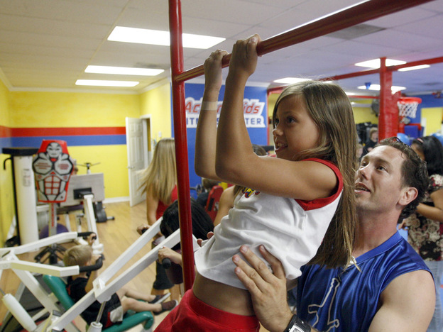 A girl does a pull-up with the help of her instructor.
