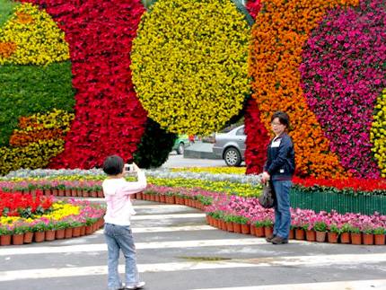 A young girl takes a picture of her mom in front of a May Day display in Chengdu, China. Photo: Melissa Block, NPR.