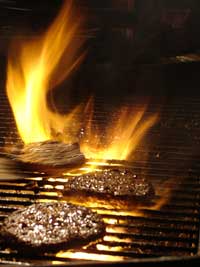 juicy hamburgers cooking on a flaming grill